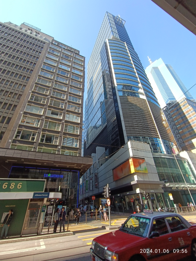 Ein rotes Auto fährt eine Stadtstraße entlang, die von hohen Wolkenkratzern gesäumt ist, mit Passanten, Verkehrszeichen und verschiedenen Schildern.
