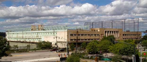 Eine breite Straße mit Fahrzeugen, gesäumt von Bäumen und Straßenlaternen, die zu einem großen Gebäude in der Nähe eines Gewässers führt.