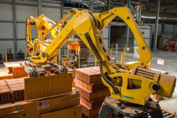 Ein großes Lagerhaus voller numerous boxes, Kräne und diverser industrieller Ausrüstung, mit einem Zaun und Polen im Vordergrund und einer Wand im Hintergrund.