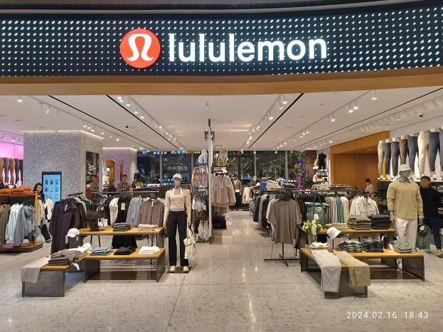 Das Innere eines lululemon-Ladens in Singapur mit Schaufensterpuppen in aktuellen Modellen, Kleidung an Bügeln und Tischen mit verschiedenen Artikeln, alles unter Deckenbeleuchtung und einem Namenbrett mit Text, mit einem Wasserzeichen auf dem Bild.