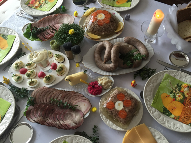 Ein langer Esstisch mit verschiedenen Speisen, Besteck und Kerzen, umgeben von Stühlen, der eine traditionelle deutsche Oster-Mahlzeit andeutet.