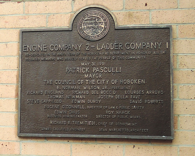 Ein rechteckiges Schild an einer Backsteinwand mit schwarzem Hintergrund und weißer fettgedruckter Schrift, die "Engine Company 2 Ladder Company" lautet.