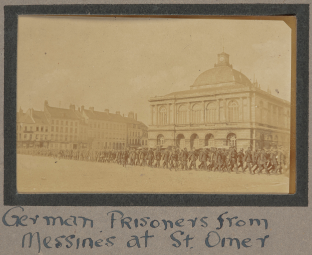 Eine Gruppe deutscher Kriegsgefangener aus Messines steht vor einem Gebäude unter einem klaren blauen Himmel, mit sichtbarem Text am unteren Bildrand.