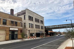 Eine Stadtstraße mit Gebäuden, Fahrzeugen, Straßenlaternen, Bäumen und einer Brücke, mit einem alten Gebäude im Vordergrund.