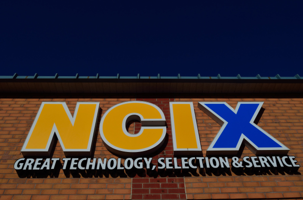 Ziegelbau mit einem Schild, auf dem "NCIX Great Technology, Selection & Service" steht, vor einem klaren blauen Himmel.