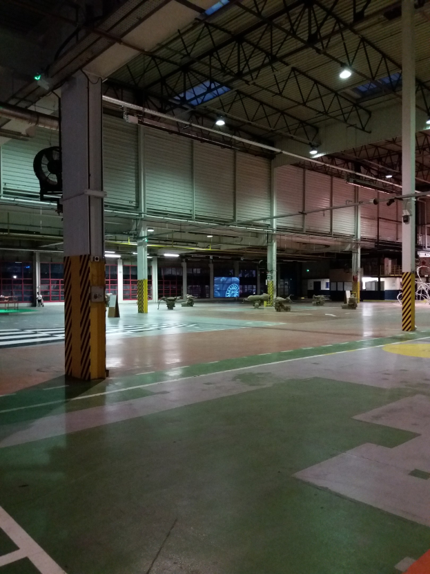 Große Lagerhalle mit diverser Maschinerie, Metallstangen und Beleuchtung; Text ist auf dem Boden auf der rechten Seite sichtbar.