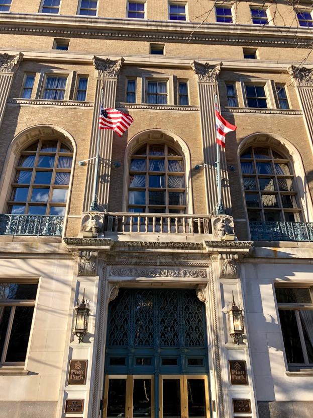 Großes Glasfrontgebäude mit mehreren Säulen, Geländern und beleuchteten Schildern mit Text, das die Plaza Hotel in New York City zeigt.