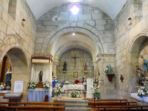 Innenansicht einer Kirche mit zahlreichen Skulpturen und Blumenpflanzen zwischen leeren Holzbänken.