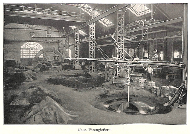Schwarzes und weißes Foto eines Fabrikinneren mit Arbeitern, die an Maschinen arbeiten, umgeben von Metallstangen und -pfählen, beschriftet mit "Neue Eisenglebeerei, die erste Fabrik in Deutschland" unten.