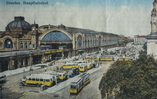 Schwarz-weiß-Postkarte des Dresdner Hauptbahnhof-Bahnhofs in Deutschland, die eine belebte Straßenszene mit Fahrzeugen, Fußgängern, Bäumen, Gebäuden und einem bewölkten Himmel zeigt.