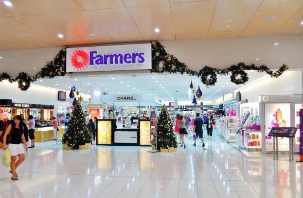 Eine Gruppe von Menschen geht durch ein Weihnachtsdekorationen Shopping-Mall mit beleuchteten Tannenbäumen, Dekorationen und einer Texttafel an der Decke, einige mit Handtaschen.