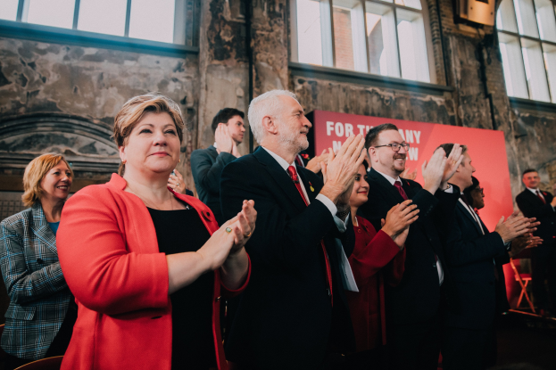 Leute klatschen feiernd vor einer Menge, mit einem Banner im Hintergrund, das einen Wahlsieg anzeigt.