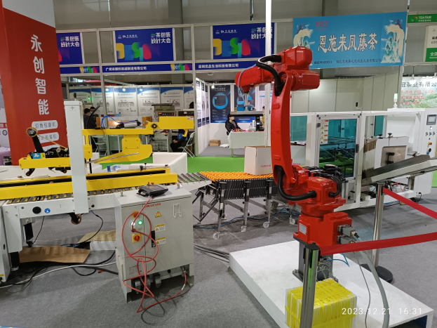 Gruppe von Robotern auf einem Tisch in einer Fabrikumgebung mit Maschinen, Kabeln, beschrifteten Platinen und Lichtern im Hintergrund sowie einigen Menschen.