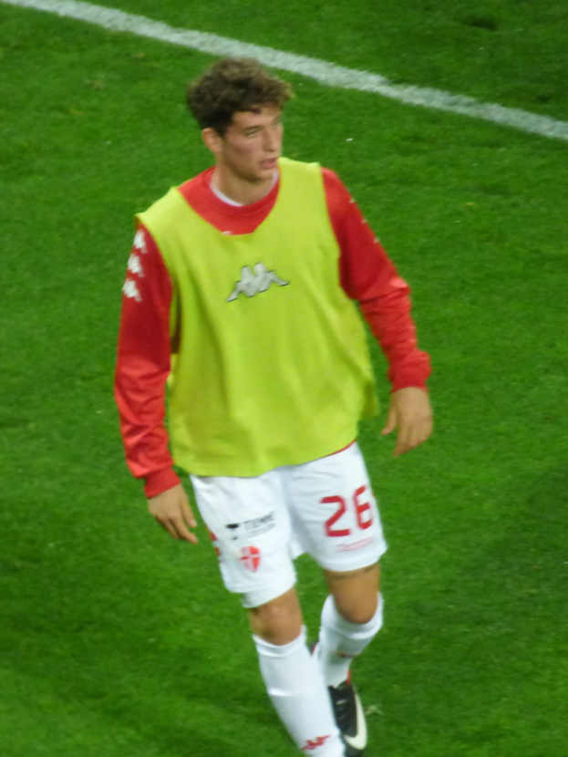 Ein Mann in einem gelben und roten T-Shirt läuft auf einem Fußballfeld, das mit weißen Linien markiert ist und trägt Fußballschuhe.