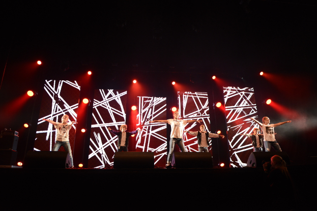 Menschen auf einer Bühne mit Scheinwerfern und anderen Gegenständen im Hintergrund.
