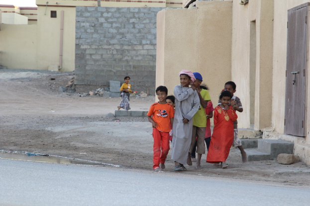 Eine Gruppe lachender Kinder, die gemeinsam auf einem Bild mit Gebäuden, Wasser, Felsen und einer Straße posieren.