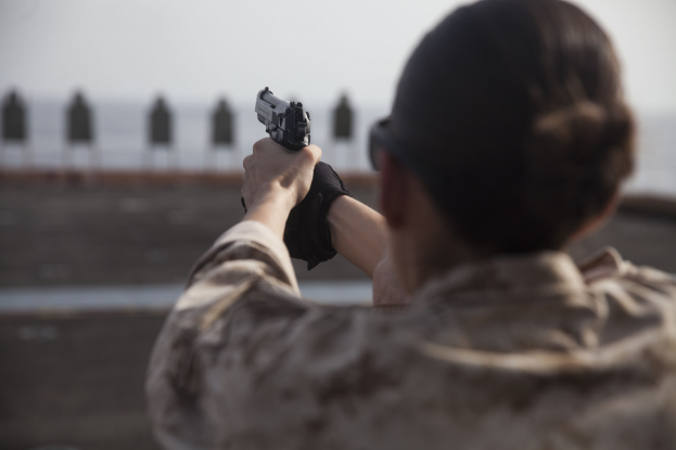 Ein Mann in militärischer Uniform zielt mit einer Pistole auf ein Ziel mit einem unscharfen Hintergrund.