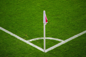 Ein Fußballfeld mit grünem Gras, weißen Begrenzungslinien und einem weißen Pfosten mit einer roten und weißen Flagge auf dem zentralen Strafstoßpunkt.