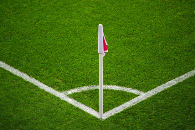 Ein Fußballfeld mit grünem Gras, weißen Begrenzungslinien und einem weißen Pfosten mit einer roten und weißen Flagge auf dem zentralen Strafstoßpunkt.