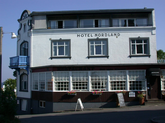 Hotel Nordland-Gebäude in Stavanger, Norwegen, mit Fenstern, einem Schild, einem Straßenpfosten, Bäumen und einem bewölkten Himmel.