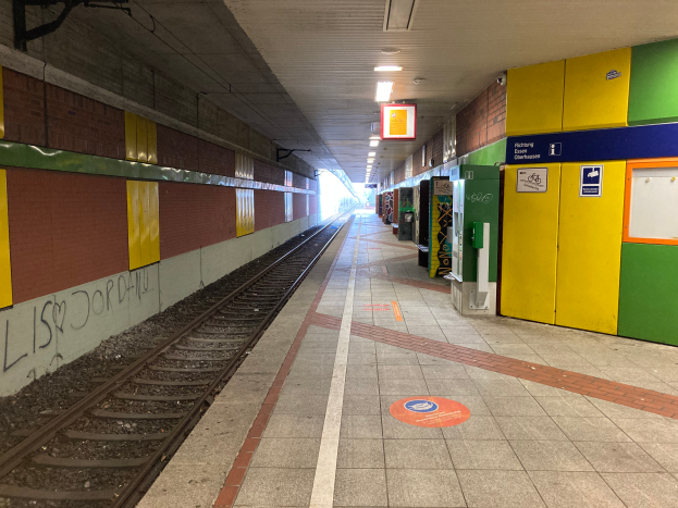 Ein Bahnhof in Berlin, Deutschland, mit einem Zug auf den Gleisen, beleuchtet von Deckenleuchten, Graffiti an der linken Wand und ein paar Gegenständen auf der rechten Seite.