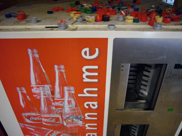 Eine Maschine mit einem Plakat, das Bilder und Text zeigt, und Flaschenverschlüssen darüber.