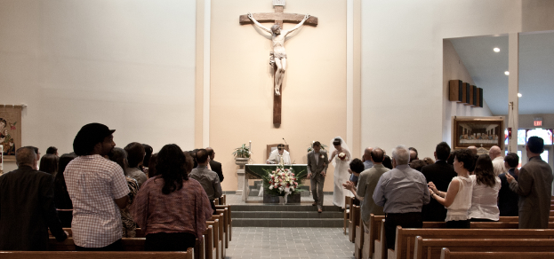 Eine kleine Gruppe von Menschen nimmt an einer Hochzeitszeremonie vor einer Wand mit einer Statue des Jesus Christus teil.