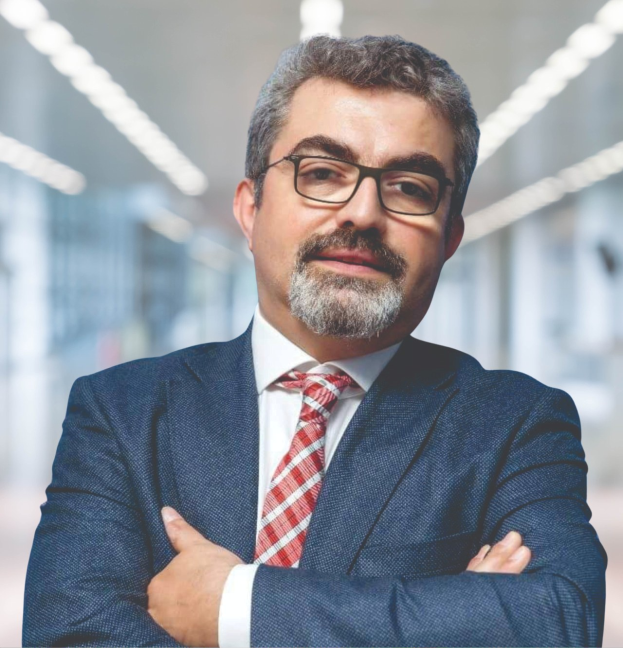 Ein Mann im Anzug und Krawatte mit verschränkten Armen, der eine Brille trägt und vor einem unscharfen Hintergrund steht, als neuer Marketingchef bezeichnet.