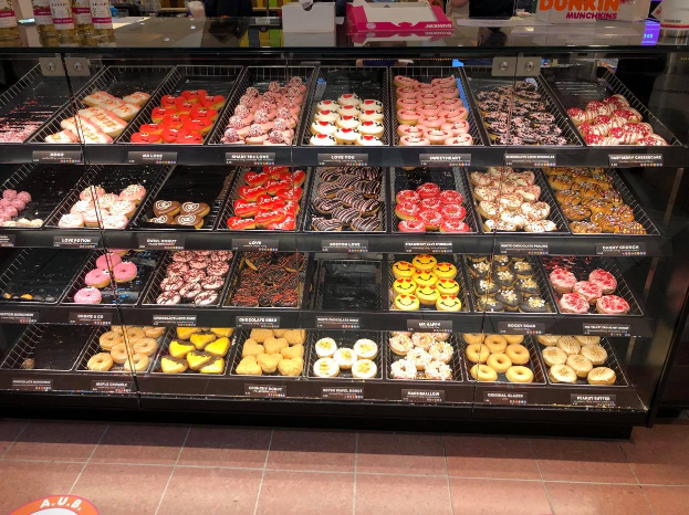 Eine Vitrine voller verschiedener Donut-Sorten, mit ein paar Menschen und Flaschen im Hintergrund.