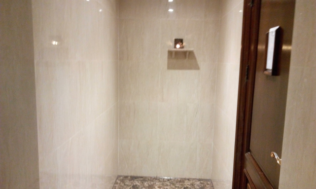 Ein Badezimmer mit Duschvorhang, Toilette und gefliesten Wänden, mit Deckenleuchten und einer Tür auf der rechten Seite.