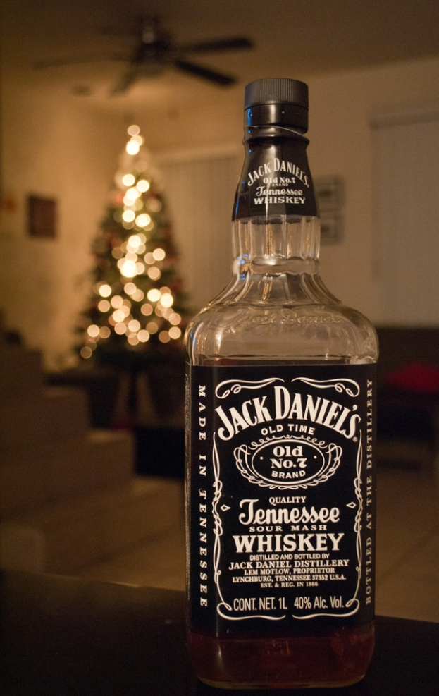 Eine Glasflasche Jack Daniel's auf einem Tisch mit einem beleuchteten Weihnachtsbaum und einem Ventilator im Hintergrund vor einer weißen Wand.