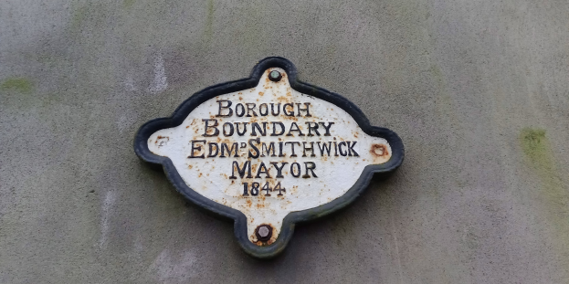 Metallschild an einem Gebäude, das die Borough-Grenze markiert, mit "Edm Smithwick Mayor" in fetter weißer Schrift auf schwarzem Hintergrund.