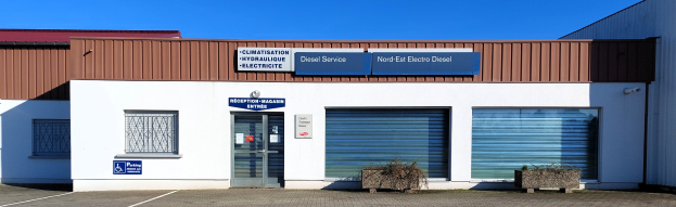 Gebäude mit einer Tafel, die "Nord-Ost-Elektro-Diesel-Service" lautet, einer Tür, Fenstern mit Rollläden, Topfpflanzen, einem Weg und einem bewölkten Himmel.