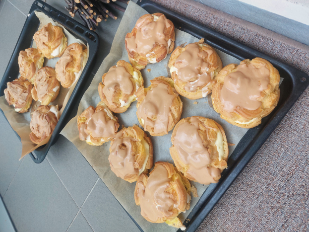 Ein Tablett mit verschiedenen Danish Pastries, einige davon mit Puderzucker bestäubt, steht auf einer Theke neben einem offenen Fenster und wird von warmem Licht durchflutet.