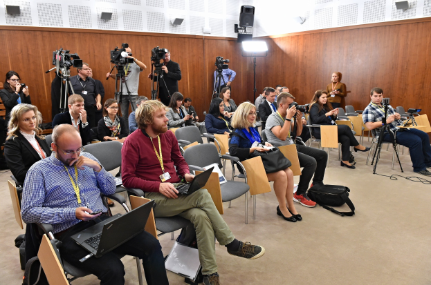 Eine Gruppe von Menschen, die mit Laptops und Kameras auf einer Konferenz über die Zukunft des Internets sitzen, mit Beleuchtung und Lautsprechern im Hintergrund.