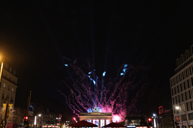 Eine belebte Stadtstraße in Berlin, Deutschland, mit dem Brandenburger Tor im Hintergrund und Feuerwerk, das den Nachthimmel erhellt.