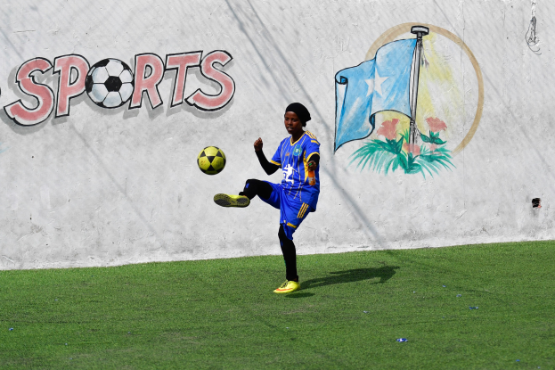 Ein junger Junge, der einen Fußball auf einem grünen Feld kickt, mit einer Wand im Hintergrund.