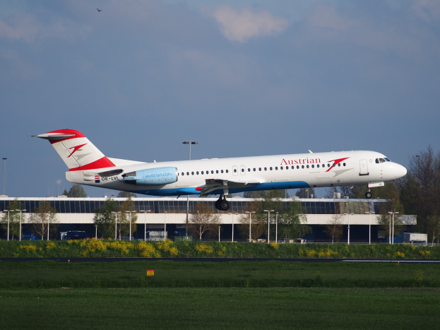 Ein Austrian-Airlines-Airbus-A320-200 beim Abheben vom Frankfurter Flughafen mit Grünflächen, Leuchten, einem Gebäude und einer bewölkten Himmel im Hintergrund.
