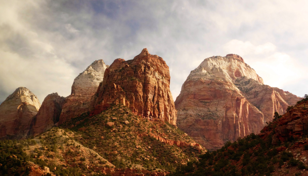 Ein Panoramablick auf den Zion-Nationalpark in Utah mit majestätischen Bergen, grünen Bäumen, felsigem Gelände und einem Himmel mit weißen Wolken.