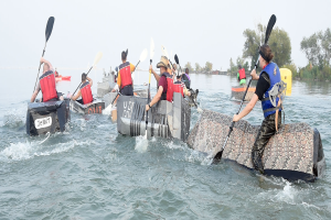 Eine Gruppe von Menschen in Schwimmwesten, die Kanus auf einem von B├Ąumen umgebenen Fluss paddeln, einige halten Paddel, was auf einen Kanurennsport hindeutet.