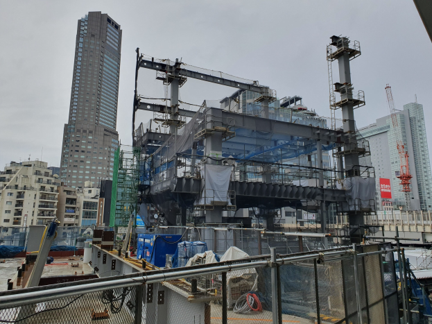 Großbaustelle für ein neues Kraftwerk in einer Stadt, umgeben von einem Metallzaun, mit Gebäuden, Polen, einer Fahne, Fahrzeugen, Drähten und einem bewölkten Himmel.