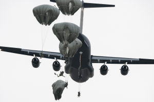 Großes Militärflugzeug mit mehreren Fallschirmen im klaren blauen Himmel