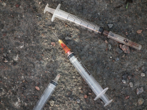 Mehrere Spritzen und eine Nadel liegen auf dem Boden verstreut.