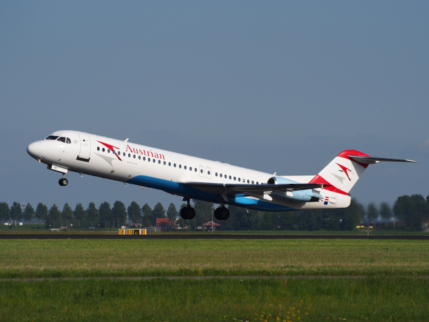 Ein Austrian Airlines Embraer ERJ-190-Flugzeug startet vom Frankfurter Flughafen, mit grünem Gras, Bäumen, Gebäuden und Himmel.