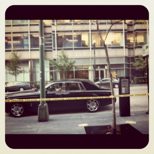 Ein Auto ist in der Mitte eines Bildes mit Pfählen und Bäumen geparkt, mit einem Gebäude, Fahrzeugen, Bäumen, Pflanzen und Lichtern im Hintergrund und einem Weg am Boden.