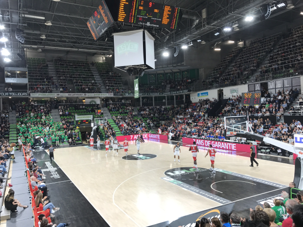Basketballspiel zwischen Asvel und Galatasaray in einem vollen Indoor-Stadion mit Zuschauern, Anzeigetafeln und Deckenbeleuchtung.