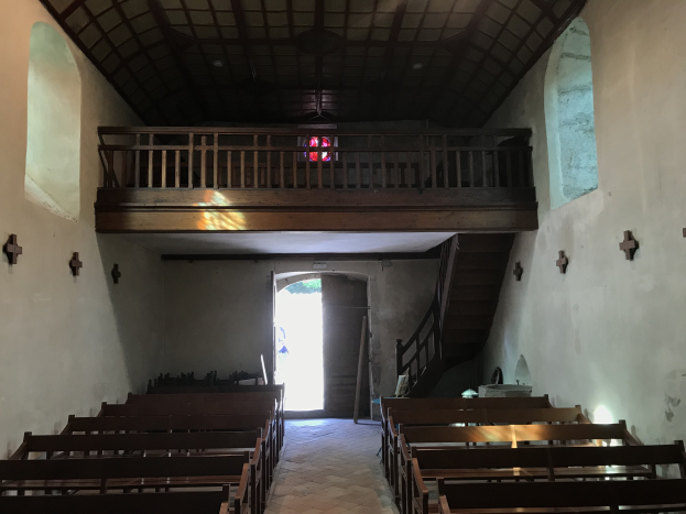 Innenraum einer Kirche mit hölzernen Kirchenbänken, gefliestem Boden, Kreuzen an den Wänden, Geländern, Treppen mit Geländern, einer Hintertür und einem Bleiglasfenster.