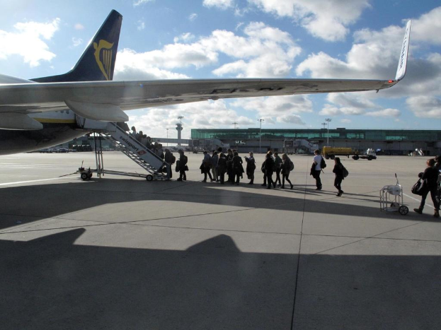Ein Flugzeug auf der Rollbahn mit einer Gruppe von Menschen, Fahrzeugen, Polen, Lampen und einem Wagen in einem Flughafen, mit dem Himmel im Hintergrund.