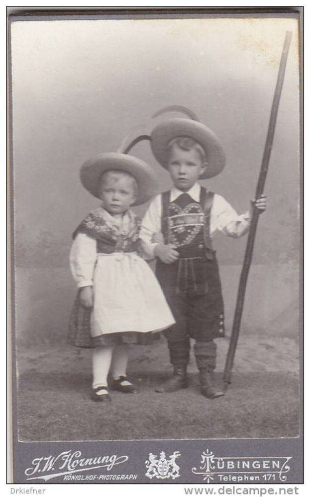 Zwei Kinder in traditioneller bayerischer Tracht, eines hält einen Stock, auf einem Schwarz-Weiß-Foto mit Text am unteren Rand.