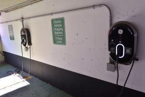 Ein Elektrofahrzeug-Ladestation in einer Tiefgarage mit zwei an der Wand angebrachten Ladesäulen und Tafeln mit Texten darauf, der Boden ist unten im Bild sichtbar.